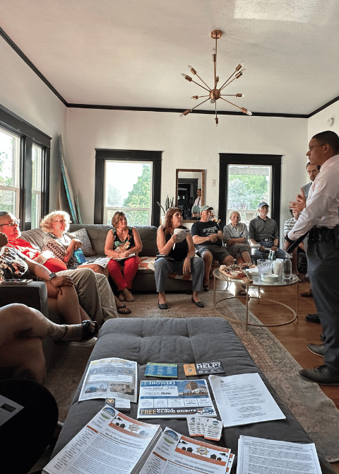 After the First Neighborhood Watch Meeting. A group of people in a living room sit on the couch and talk.